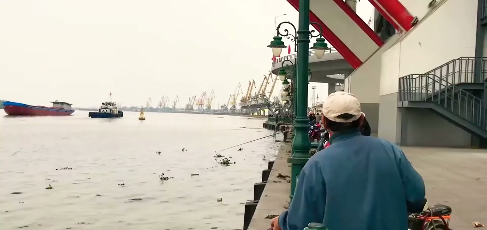Người dân câu cá dưới chân cầu Hoàng Văn Thụ Hải Phòng, tàu kéo và sà lan chạy trên sông Cấm, dàn cần cẩu cảng xếp hàng dài phía xa